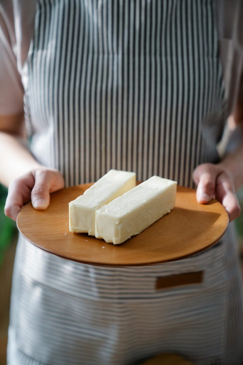 Close-up of a chef holding a wooden plate with two sticks of butter.