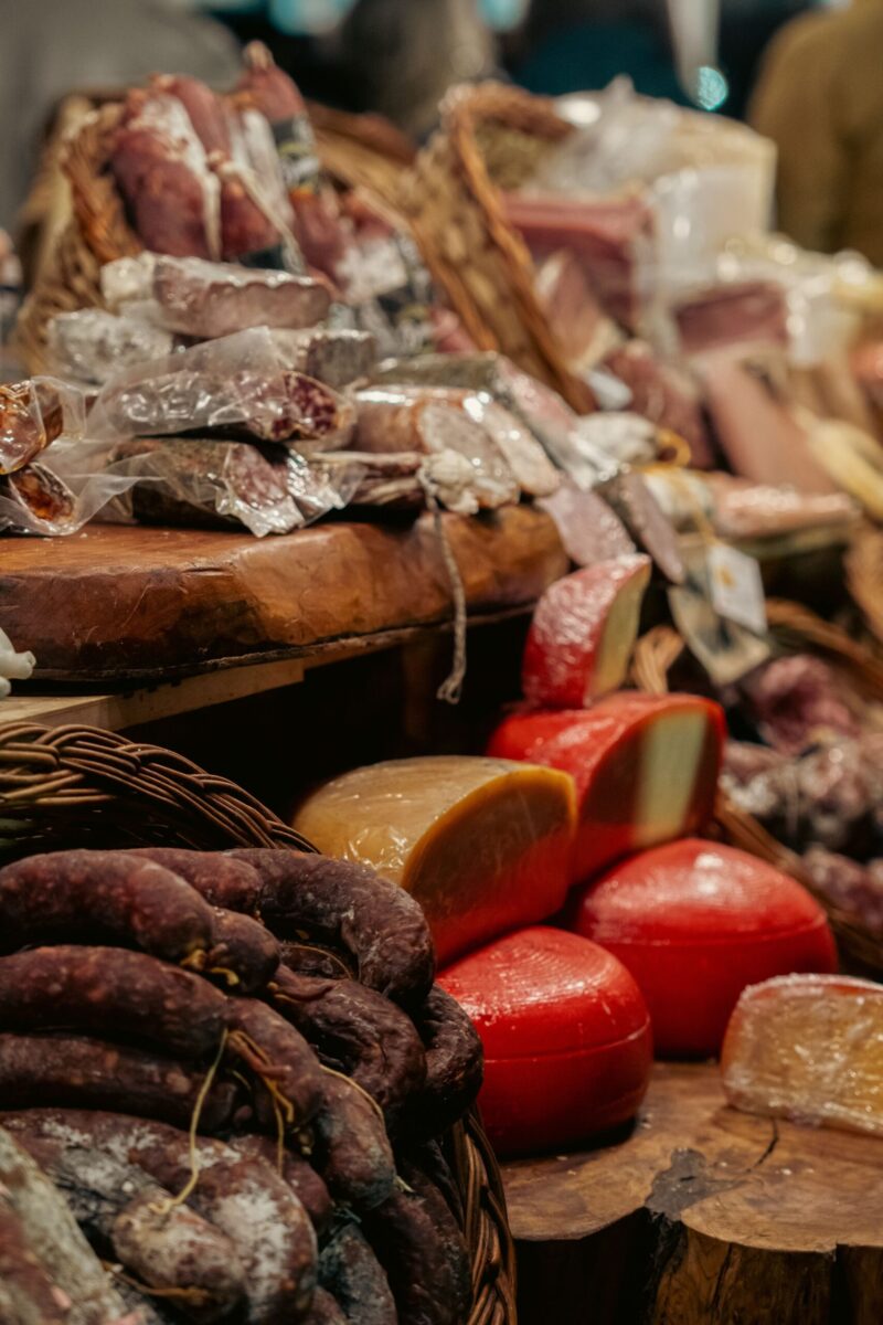 A mouthwatering display of cured meats and aged cheeses at a bustling market stall.