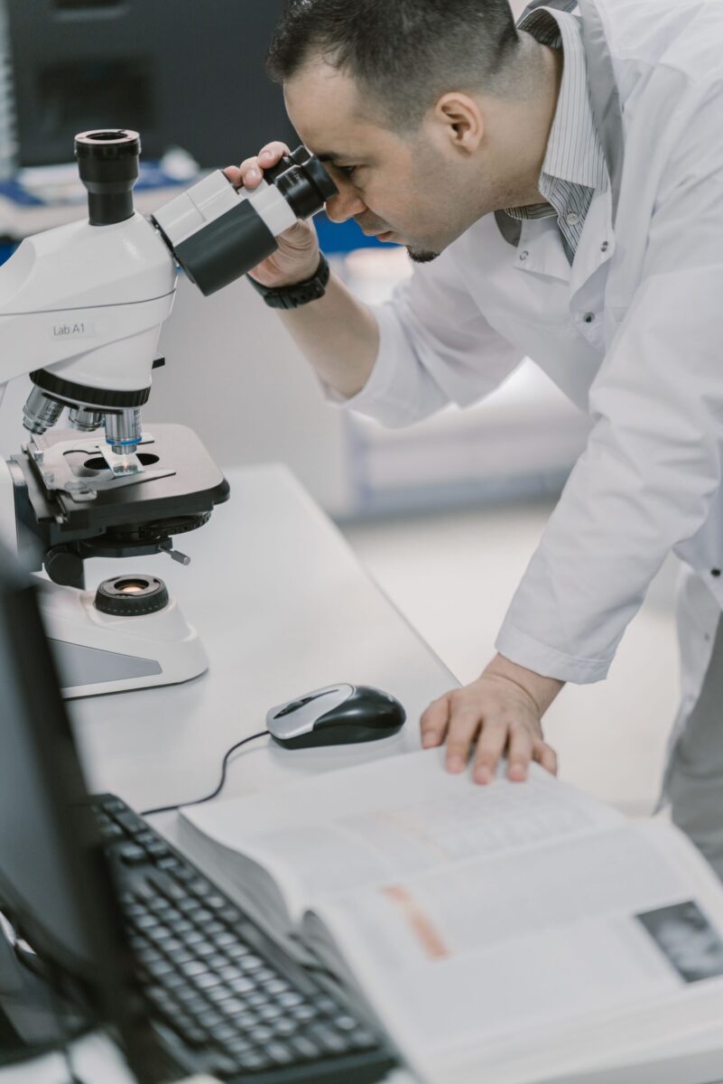 Scientist in a lab coat examines samples using a microscope. Professional laboratory environment.